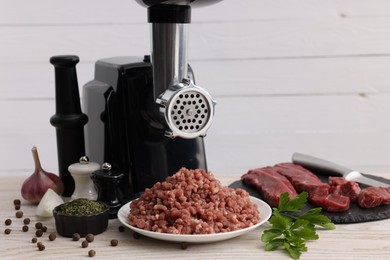 Electric meat grinder with beef, spices and parsley on white wooden table