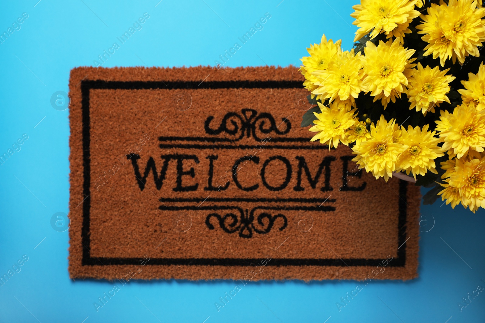 Photo of Doormat with word Welcome and flowers on light blue background, flat lay