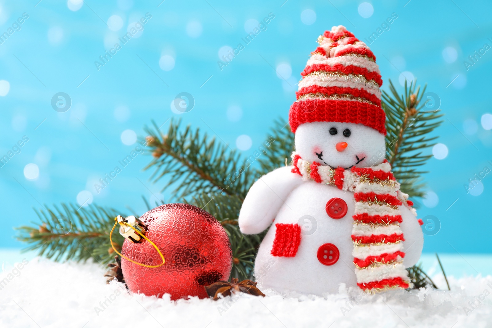 Photo of Cute toy snowman, fir branch and Christmas ball on snow against blurred background