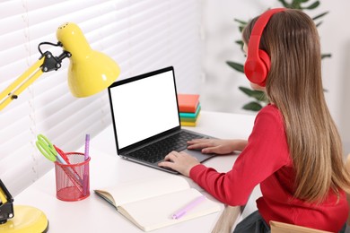 E-learning. Girl using laptop and headphones during online lesson at table indoors