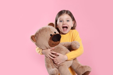 Photo of Emotional little girl with teddy bear on pink background