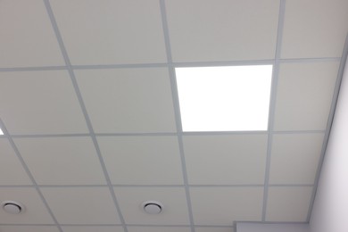 Photo of White ceiling with PVC tiles and lighting indoors, low angle view