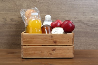 Photo of Humanitarian aid. Different food products for donation in crate on wooden table