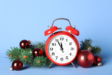 Alarm clock with Christmas decor on light blue background. New Year countdown