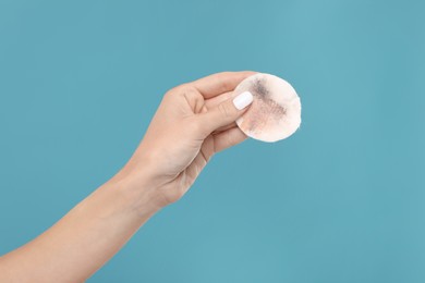 Woman with dirty cotton pad after removing makeup on light blue background, closeup