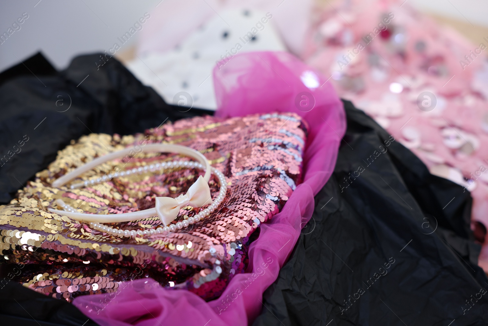 Photo of Headbands and stylish pink carnival costume with sequins in black box, closeup