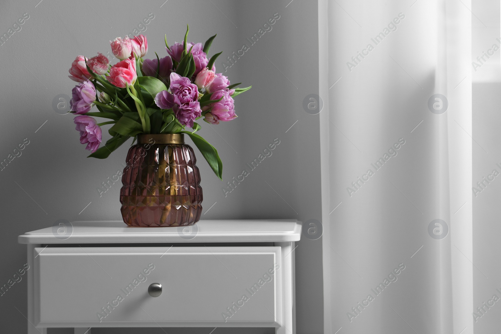 Photo of Beautiful bouquet of colorful tulip flowers on white bedside table indoors, space for text