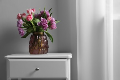Beautiful bouquet of colorful tulip flowers on white bedside table indoors, space for text