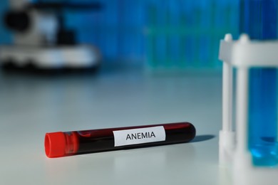 Photo of Test tube with blood sample and label Anemia on white table against blurred background. Space for text
