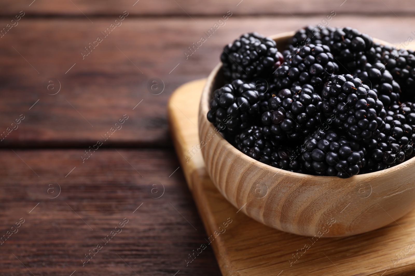 Photo of Fresh ripe blackberries in bowl on wooden table, closeup. Space for text