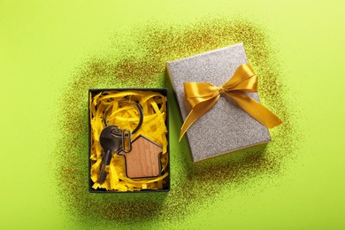Photo of Key with trinket in shape of house, glitter and gift box on light green background, flat lay. Housewarming party