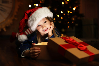 Photo of Cute child opening magic gift box near Christmas tree at night