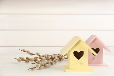 Photo of Beautiful bird houses and pussy willow branches on white wooden table, space for text