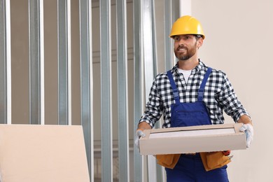 Professional builder in uniform carrying box indoors