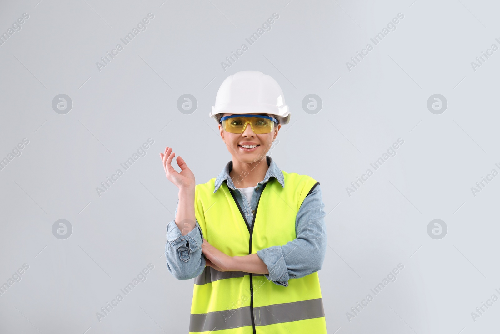 Photo of Female industrial engineer in uniform on light background. Safety equipment