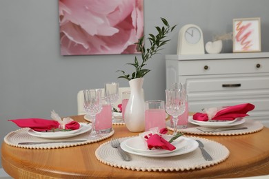 Photo of Color accent table setting. Glasses, plates, vase with green branch and pink napkins in dining room