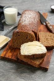 Photo of Tasty freshly baked bread with butter on grey table
