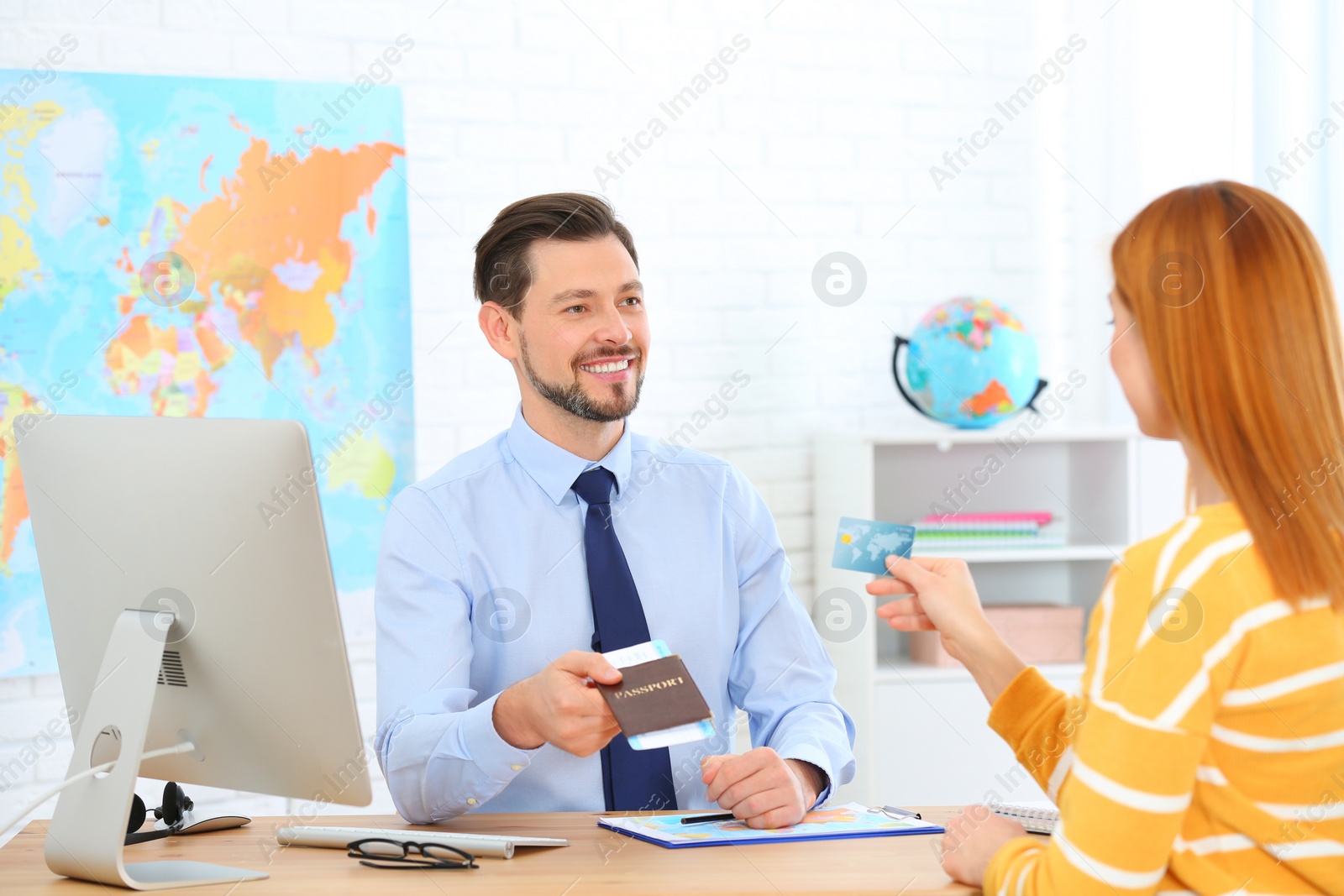 Photo of Male manager giving passport with ticket to client in travel agency