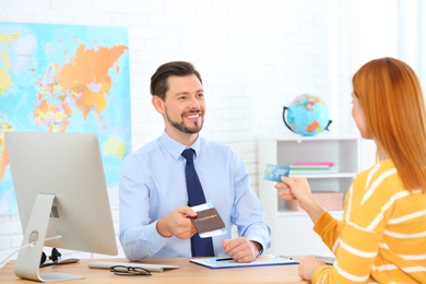 Male manager giving passport with ticket to client in travel agency