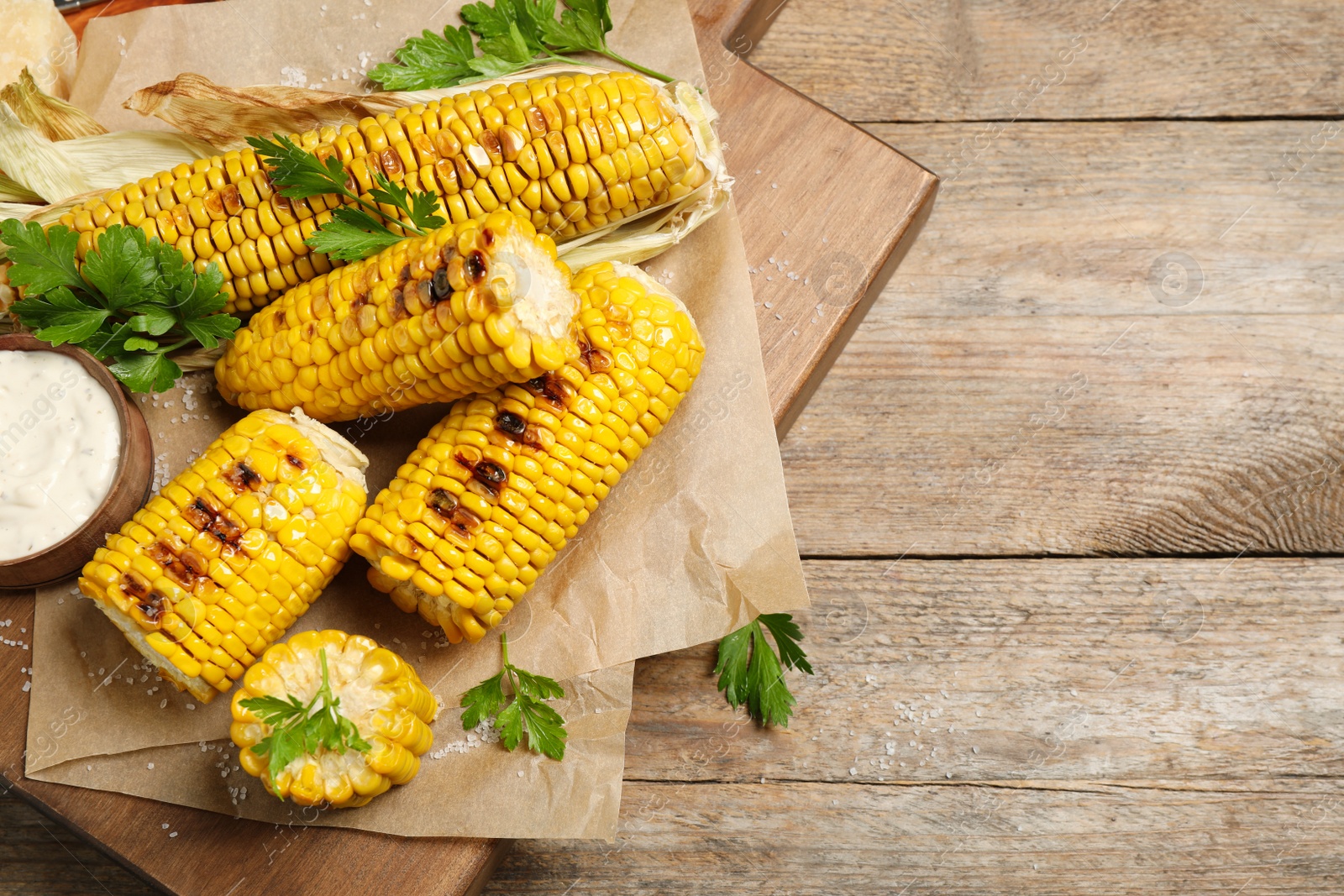 Photo of Delicious grilled corn cobs on wooden table, flat lay. Space for text