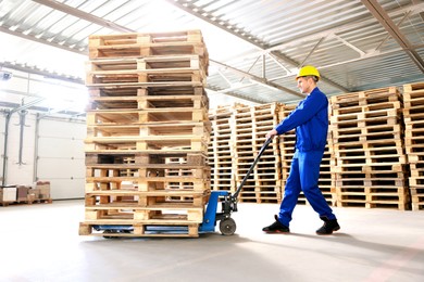 Image of Worker moving wooden pallets with manual forklift in warehouse