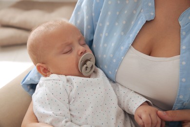 Mother holding her cute sleeping baby with pacifier indoors