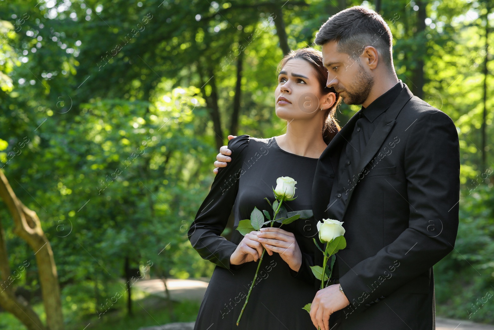 Photo of Sad couple with white rose flowers mourning outdoors, space for text. Funeral ceremony