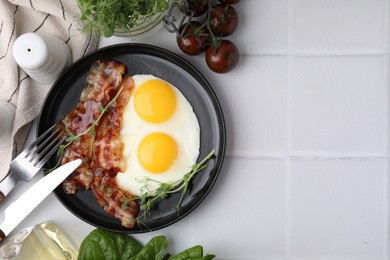 Photo of Fried eggs and bacon served on white tiled table, top view. Space for text