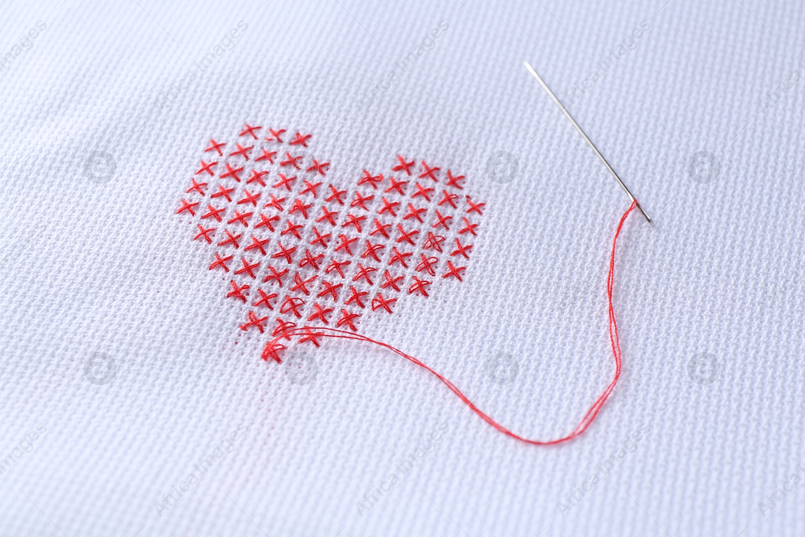 Photo of Embroidered red heart and needle on white cloth, closeup