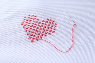 Photo of Embroidered red heart and needle on white cloth, closeup