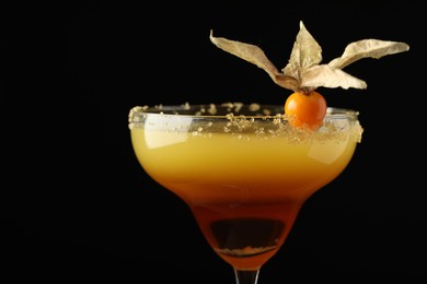 Photo of Tasty cocktail decorated with physalis fruit on black background, closeup