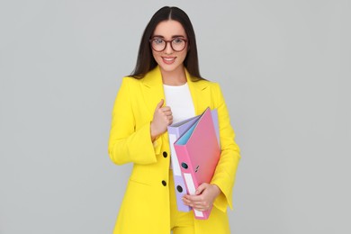 Photo of Young female intern with eyeglasses and folders on grey background