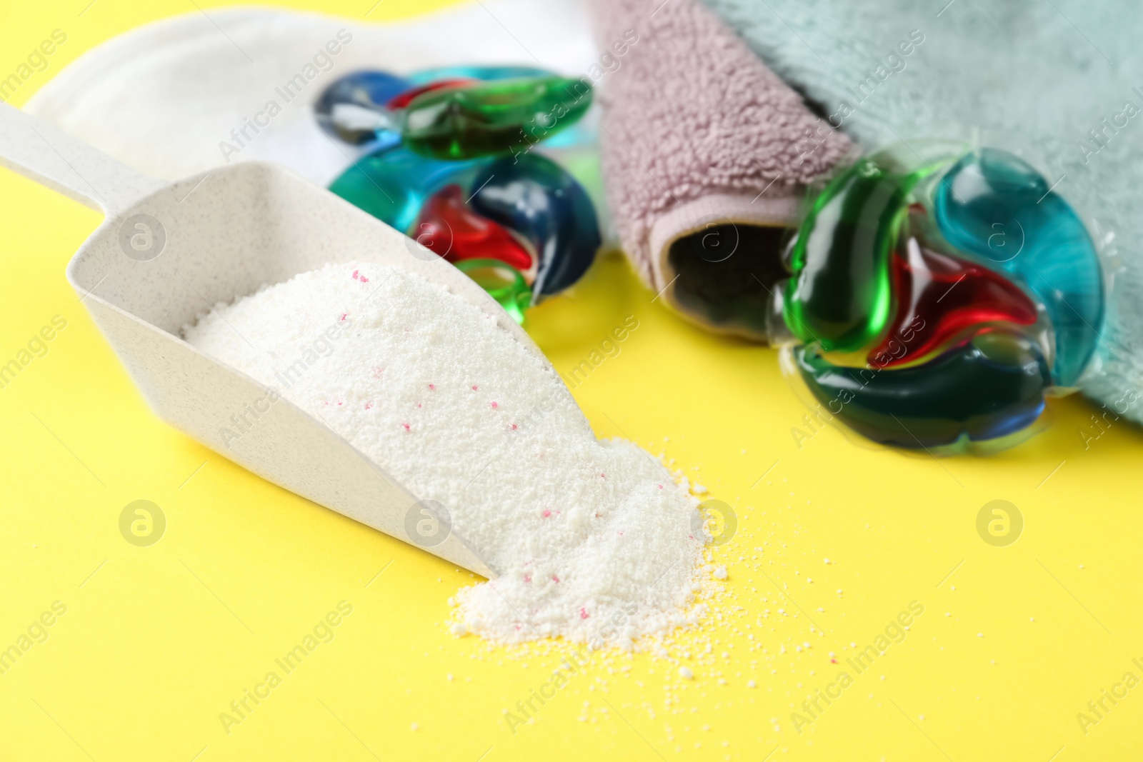 Photo of Laundry capsules, scoop of washing powder and towels on yellow background, closeup