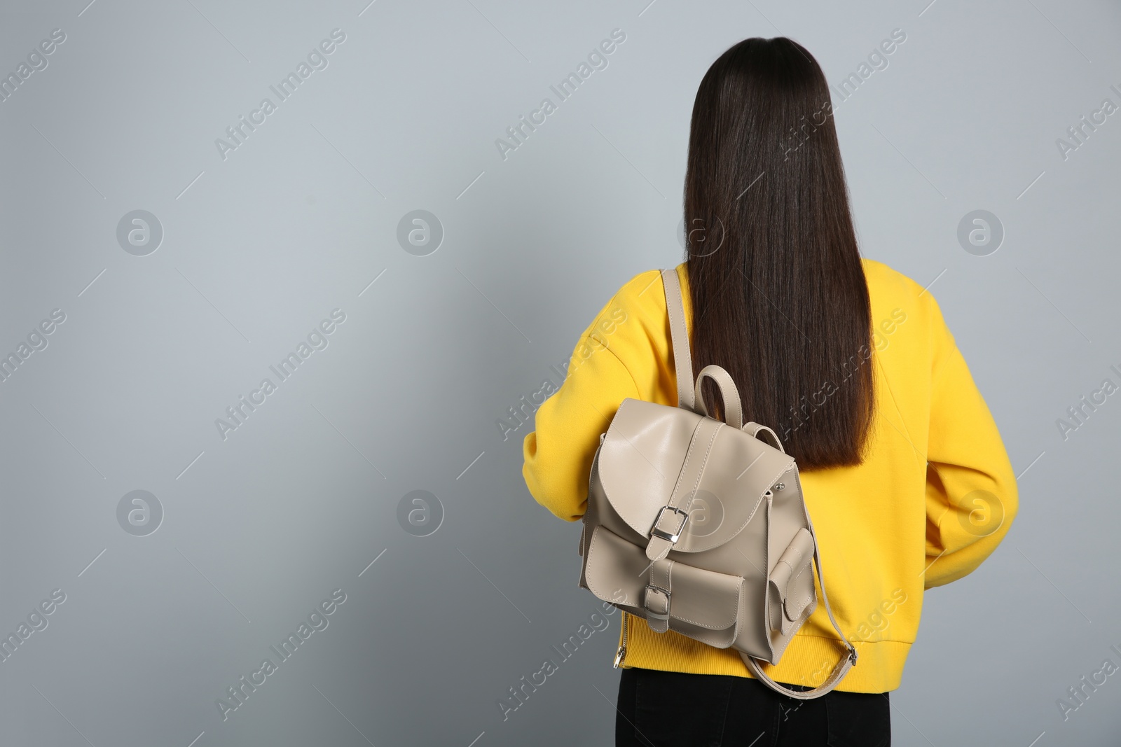 Photo of Young woman with stylish leather backpack on grey background, back view. Space for text