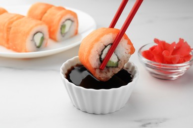 Photo of Dipping tasty sushi into soy sauce at white marble table, closeup
