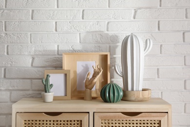 Photo of Different accessories on wooden cabinet near white brick wall indoors. Interior design