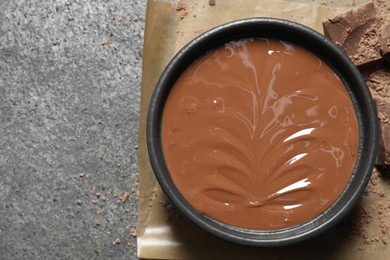 Photo of Melted milk chocolate in bowl on gray table, top view. Space for text