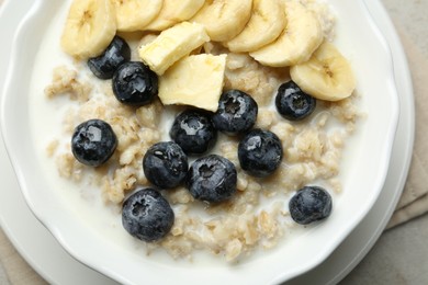 Tasty oatmeal with banana, blueberries, butter and milk served in bowl on light grey table, top view