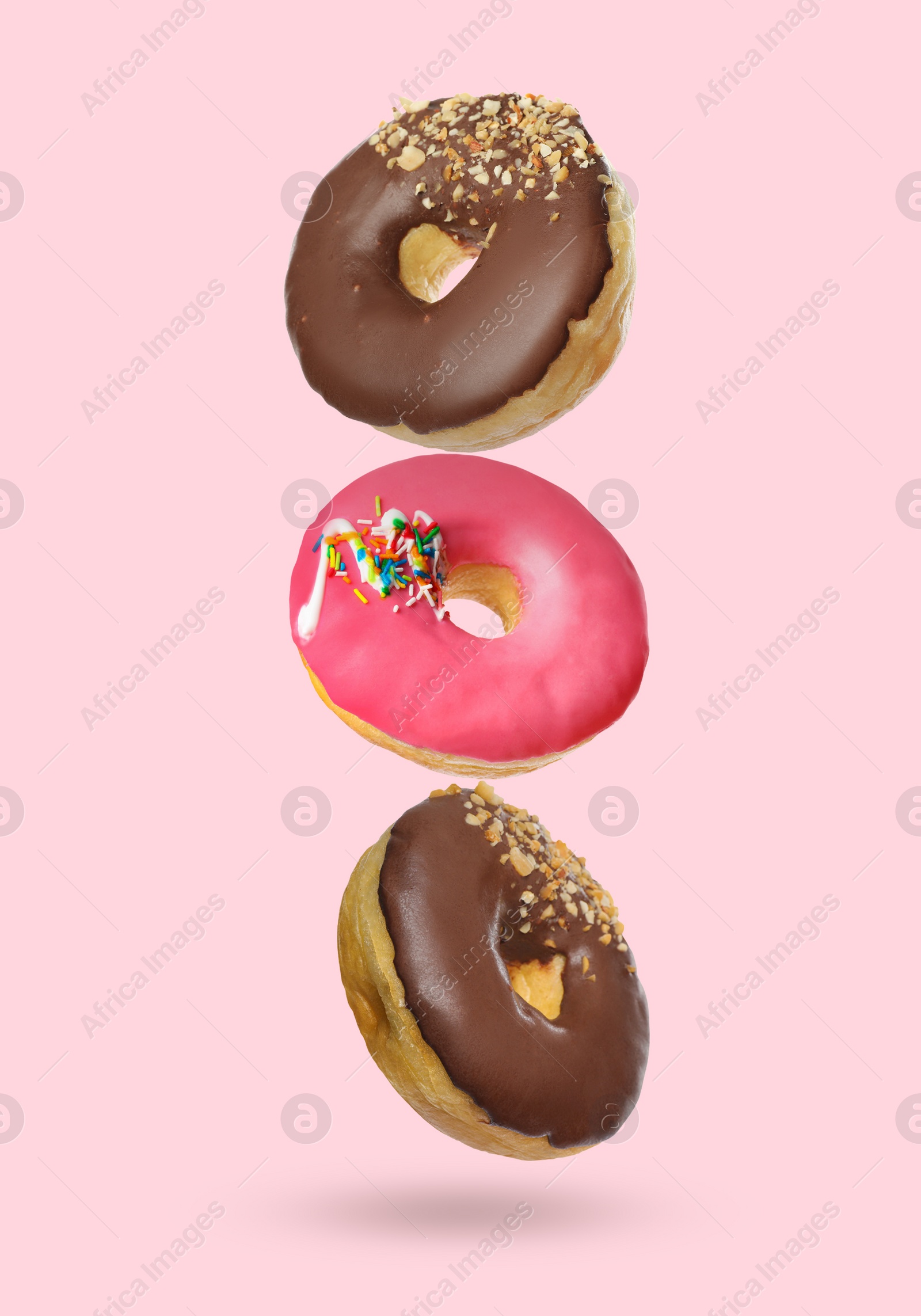 Image of Different tasty donuts falling on pastel pink background