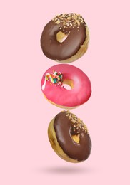 Image of Different tasty donuts falling on pastel pink background