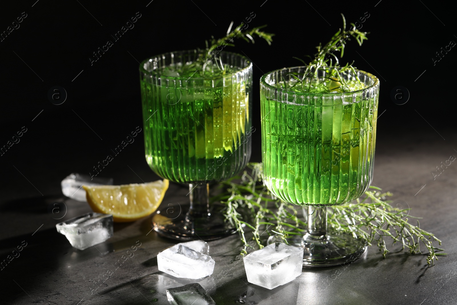 Photo of Glasses of homemade refreshing tarragon drink, ice cubes and sprigs on grey table