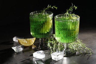 Photo of Glasses of homemade refreshing tarragon drink, ice cubes and sprigs on grey table