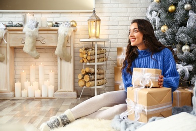 Beautiful young woman with gift boxes near Christmas tree at home