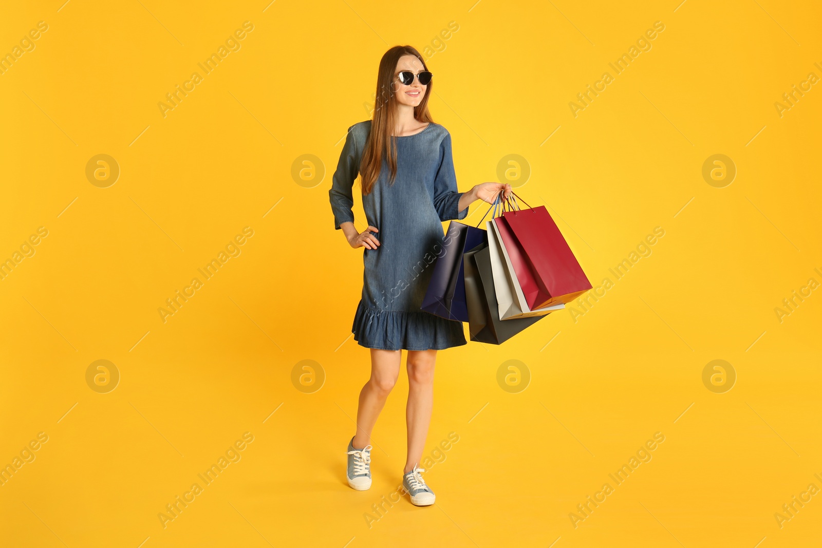 Photo of Beautiful young woman with paper shopping bags on yellow background