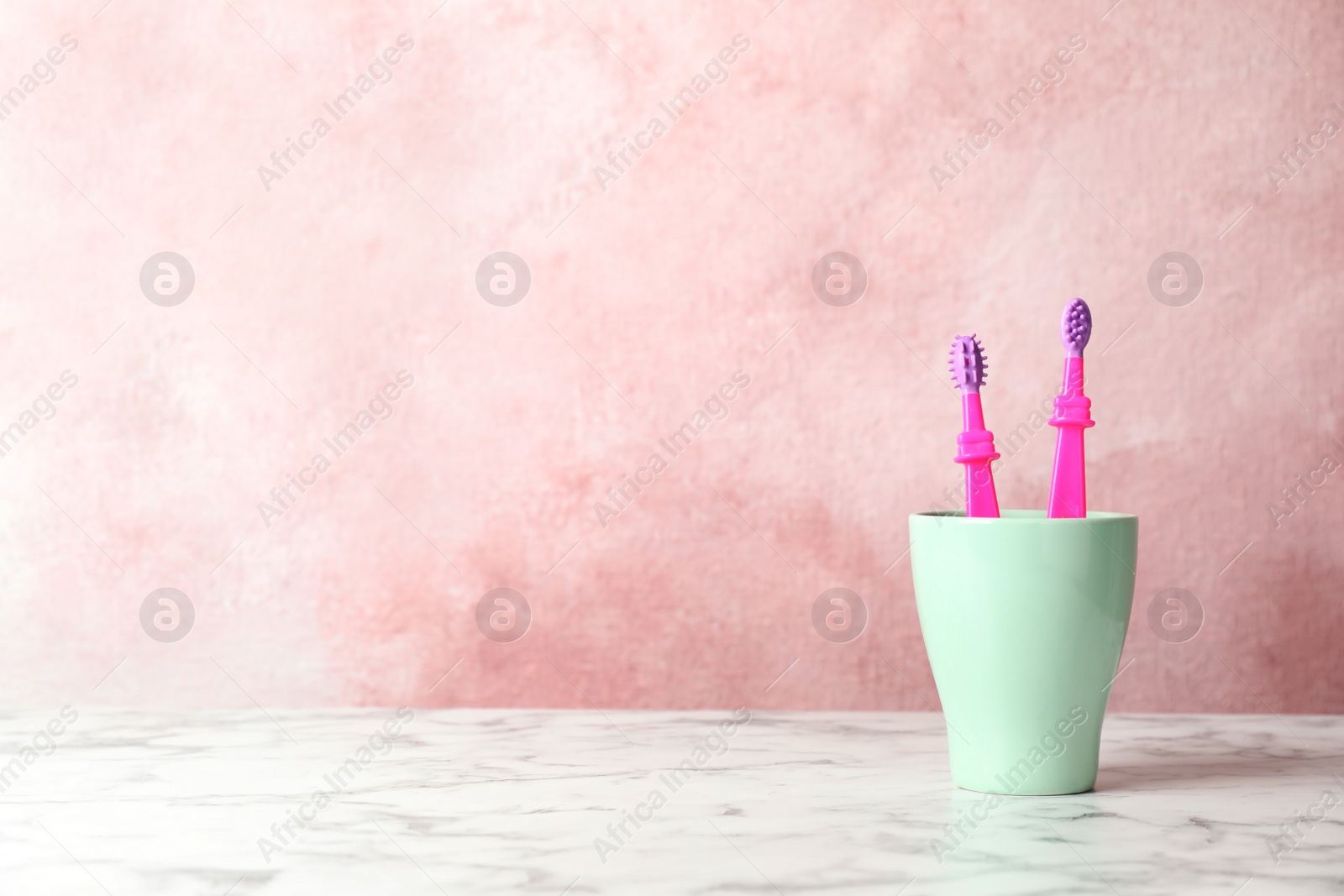 Photo of Baby toothbrushes in holder on table against color background with space for text