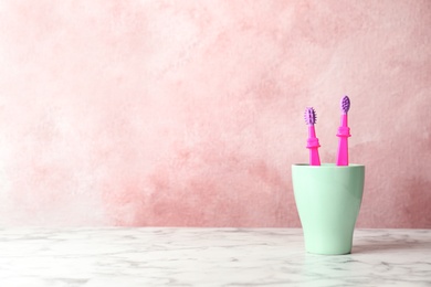 Photo of Baby toothbrushes in holder on table against color background with space for text