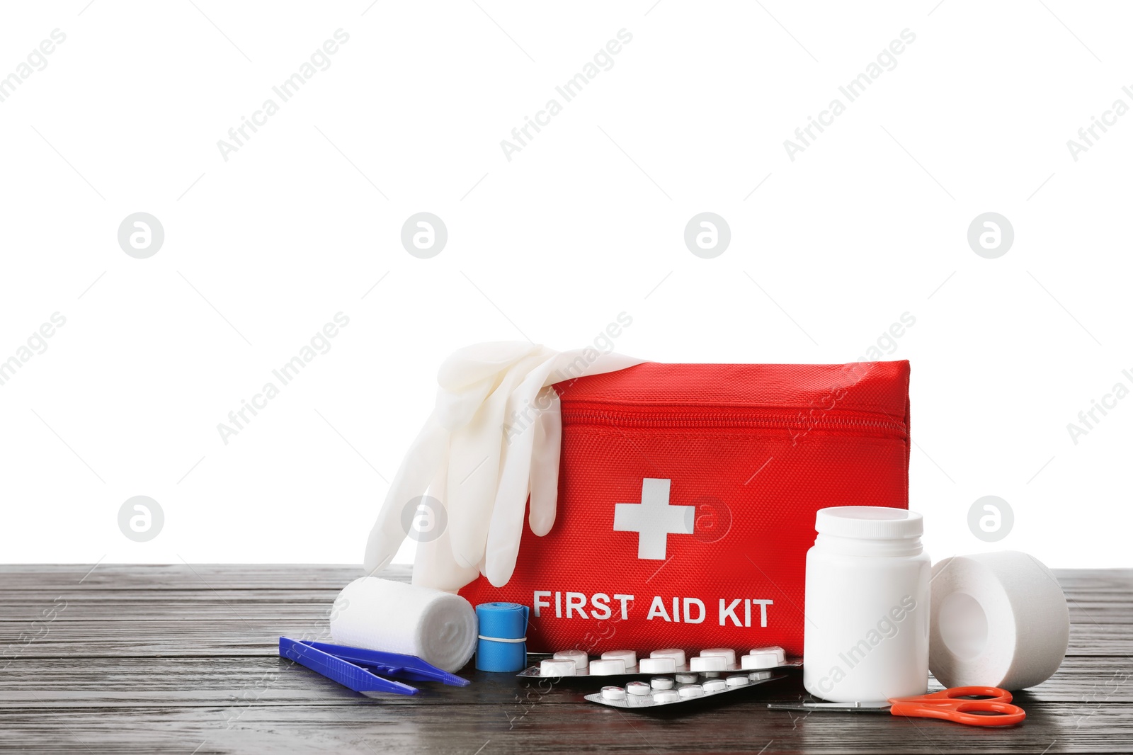 Photo of First aid kit, scissors, gloves, pills, plastic forceps and elastic bandage on wooden table against white background