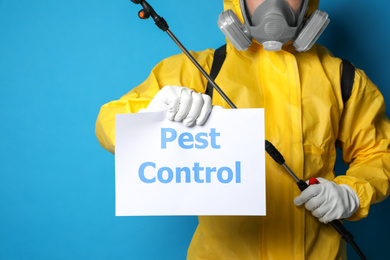 Photo of Man wearing protective suit with insecticide sprayer holding sign PEST CONTROL on blue background, closeup