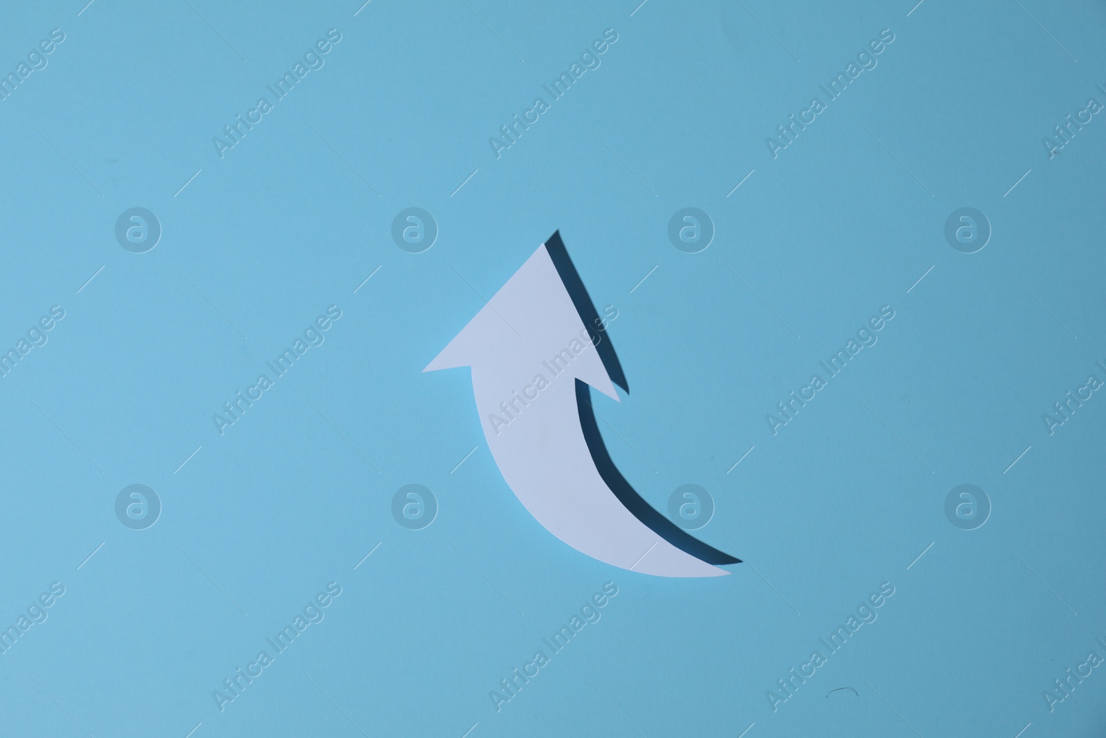 Photo of White curved paper arrow on light blue background, top view