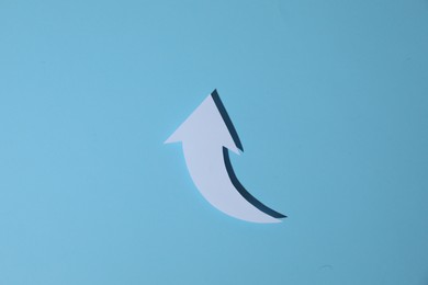 White curved paper arrow on light blue background, top view